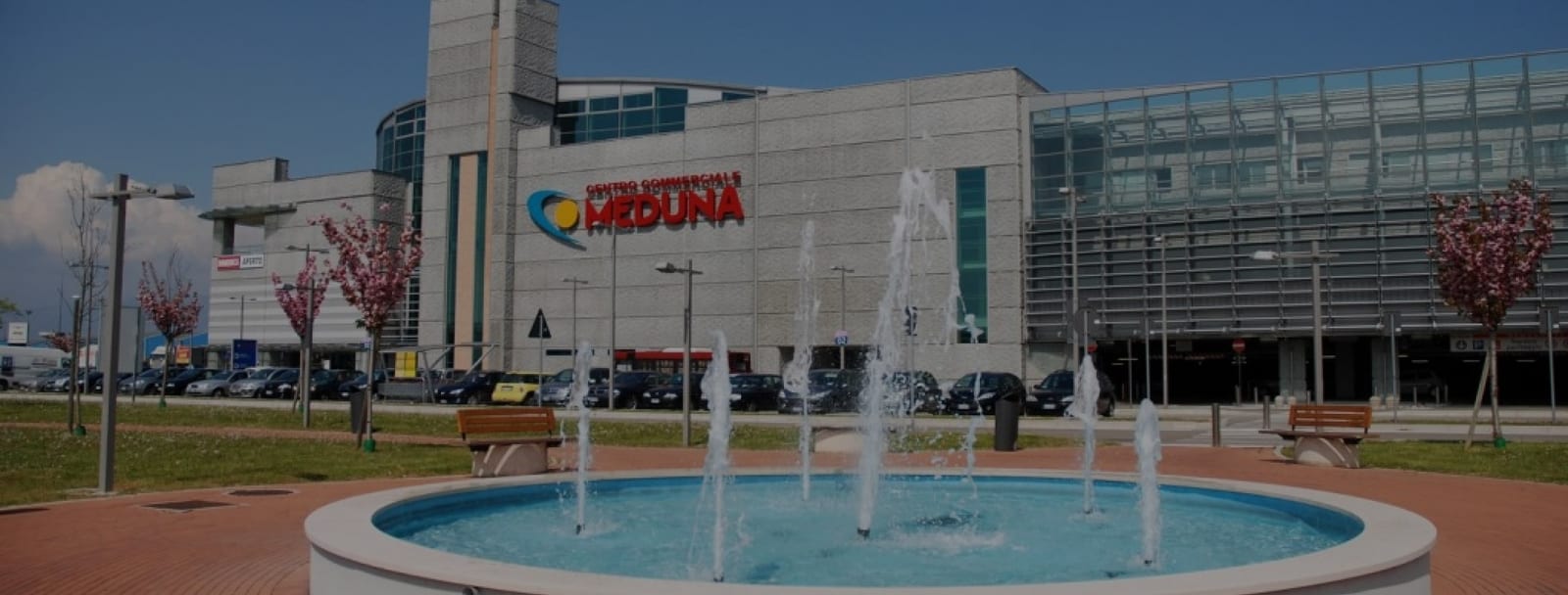 Il Centro Commerciale Meduna visto dal piazzale, con la fontana e il parcheggio davanti all'ingresso