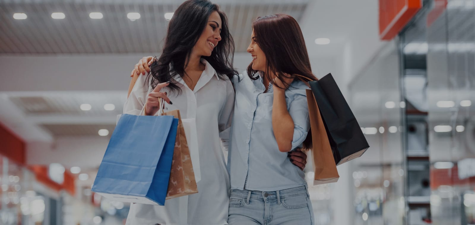 La galleria del Centro Commerciale Meduna: due ragazze camminano fra i negozi con le borse degli acquisti